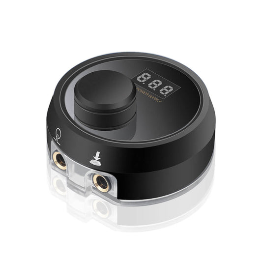 Tattoo Machine Power Supply. Black round unit with a central knob and digital display on top, and clear input ports on the side.
